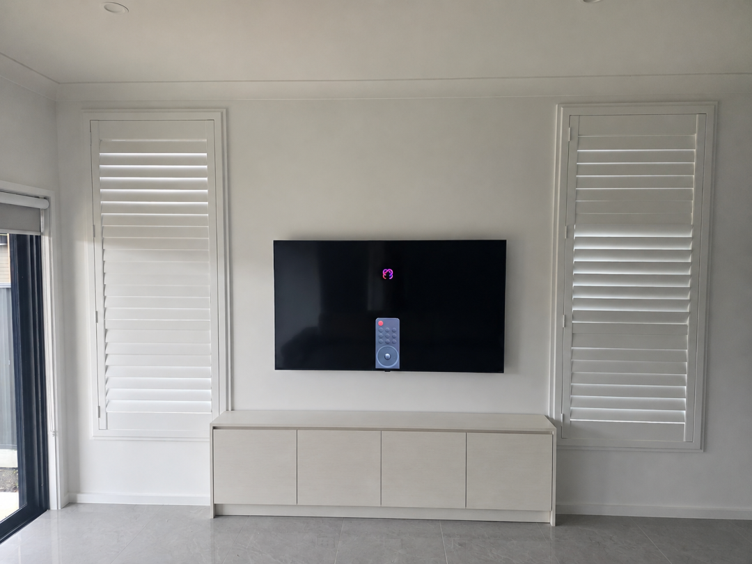 65-inch LG QNED TV wall mounted between two shuttered windows with a low cabinet below.